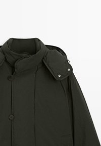 Giacca a vento verde scuro con colletto alto, bottoni e chiusure a pressione sulle spalle. Presenta una texture liscia e un design leggero.