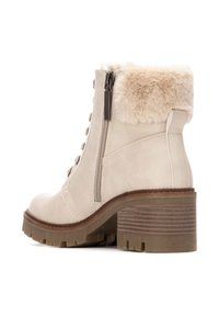 Botín beige hasta el tobillo con un cuello de faux fur texturizado, cremallera lateral, parte delantera con cordones y un tacón robusto de bloque. Suela de goma con patrones de agarre.