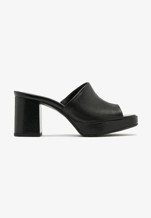 Mules de tacón abierto y negro, hechos de cuero suave. Con un tacón grueso y un diseño minimalista con una ligera plataforma.