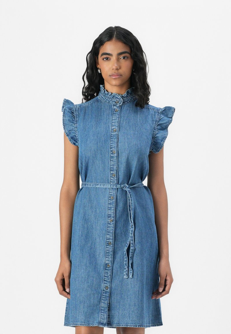 Denim mekko, jossa on röyhelöselkä, nappilista ja vyöllinen vyötärö. Vaaleansininen väri ja pehmeä rakenne. Rentoa, polvipituista muotoilua.