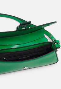 Vihreä käsilaukku kiiltävällä pinnalla, jossa on musta vuori, yläkansi, hopeinen napin sulku ja sisätasku vetoketjulla.