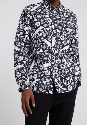 Czarna koszula na guziki z białymi abstrakcyjnymi wzorami, w tym dinozaurami, roślinami, rękami i gwiazdami, noszona z czarnymi spodniami.