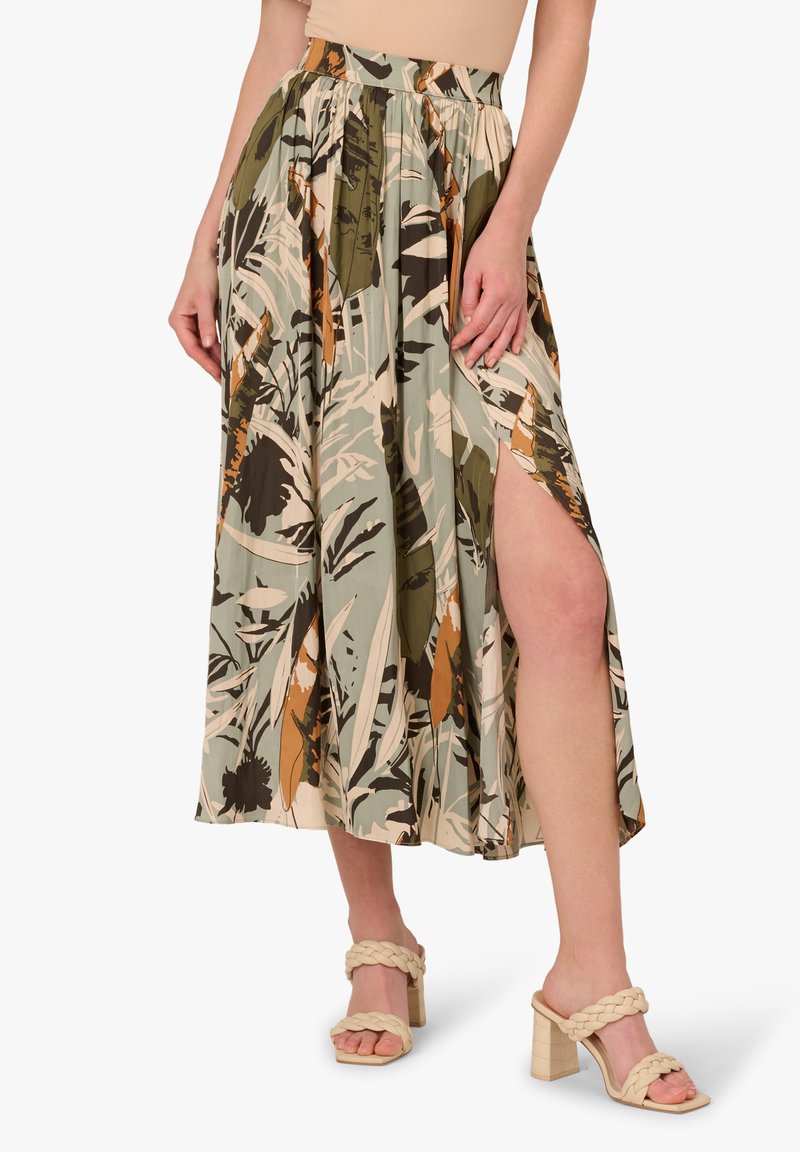 Gonna midi floreale in toni di verde, beige e marrone con un alto spacco, realizzata in tessuto leggero; abbinata a sandali con tacco e cinturini intrecciati.