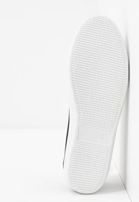 Semelle de chaussure avec motif de bande de roulement ondulé, en caoutchouc blanc, taille 38 marquée sur le talon, positionnée verticalement contre un fond blanc d'angle.