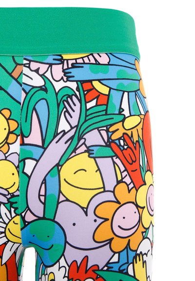 Leggings colorati con una vita verde e una stampa giocosa di fiori, facce sorridenti e mani su uno sfondo bianco.