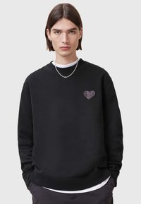 Felpa nera in cotone con scollatura rotonda, caratterizzata da un piccolo design a forma di cuore sul petto e polsini e orlo a coste.