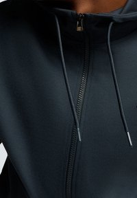 Felpa zip-up di colore blu scuro con colletto alto, dotata di zip frontale, cordini regolabili e texture di tessuto morbido.