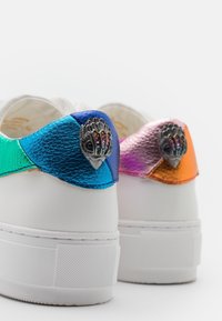 Sneakers bianchi con tacco in pelle metallica multicolore; i colori includono verde, blu, rosa e arancione, con accenti in hardware decorativo.