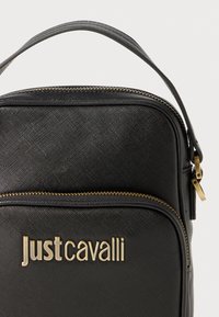 Fekete textúrájú táska arany Hardverrel, cipzáros záródással és a "Justcavalli" logó nyomott mintájával az elején. Kompakt forma, fülekkel.