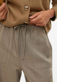 Jasnoszare, teksturowane spodnie z elastycznym paskiem, sznurkiem do regulacji i bocznymi kieszeniami. W połączeniu z brązowym, dzianym kardiganem ozdobionym guzikami w kształcie serc.