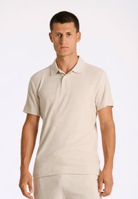 Beige pikétröja gjord av texturerat tyg, med klassisk krage, korta ärmar och tre knappar fram.