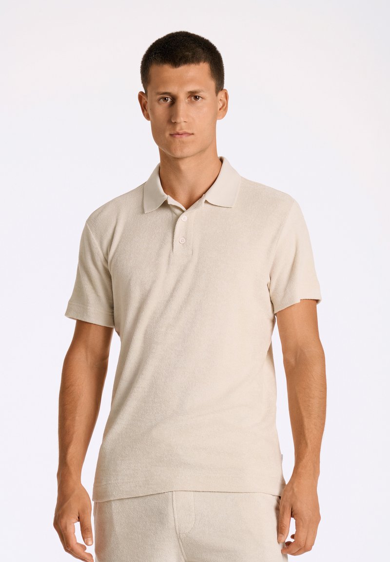 Beige pikétröja gjord av texturerat tyg, med klassisk krage, korta ärmar och tre knappar fram.