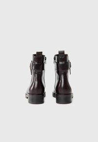 Bottines en cuir marron avec une finition lisse, dotées d'une fermeture éclair sur le côté, d'une languette à l'arrière de la tige et d'un petit talon empilé.