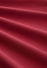 Tela roja con una superficie texturizada, que presenta pliegues suaves y patrones de tejido visibles, creando profundidad y dimensión.