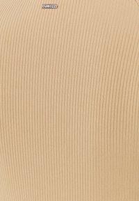 Tissu côtelé beige avec une petite étiquette métallique centrée portant la mention "CANEX" près du bord supérieur.