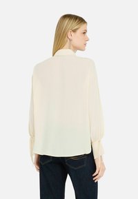 Hellbeige Bluse, lange Ärmel mit gebundenen Manschetten, lockere Passform, abgerundetem Saum, weicher Textur, ausgestattet mit Kragen und Details am Rücken.