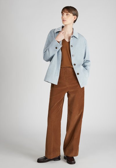 Lichtblauwe corduroy jas met een gekraagde halslijn en bruine knopen, gecombineerd met bruine wijde corduroy broek en zwarte schoenen.