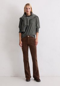 Szary longsleeve z miękkim szalem przewieszonym przez ramiona, w połączeniu z brązowymi spodniami z sztruksu w fasonie dzwonowym oraz ciemnobrązowymi butami.