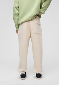 Beige sweatpants van zachte stof, met een achterzak en een elastische tailleband, gecombineerd met een lichtgroene oversized sweatshirt.
