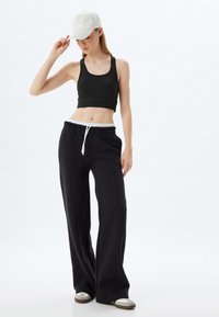 Zwarte cropped tanktop, zwarte sweats met witte drawstring en lichtgrijze pet. Zachte textuur, losse pasvorm en casual ontwerp.