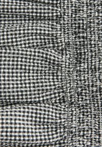 Mustvalge ruuduline kangas, mis moodustab tekstureeritud kindakujuga, nähtavate õmblustega ja kergelt kortsus randmeosaga.