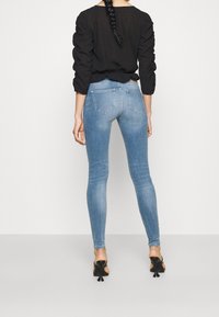 Jeans ajustados de color azul claro con una textura suave y un desvanecimiento mínimo. Tienen dos bolsillos traseros y una cintura de media altura, combinados con una camiseta negra.