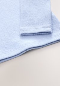 Hellblauer Sweatshirt-Stoff mit weicher Textur, ausgestattet mit einem abgerundeten Saum und Bündchenärmeln. Nähte sind entlang der Kanten sichtbar.