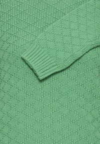Suéter verde de punto con textura en forma de diamante y detalles de puños acanalados en la manga.