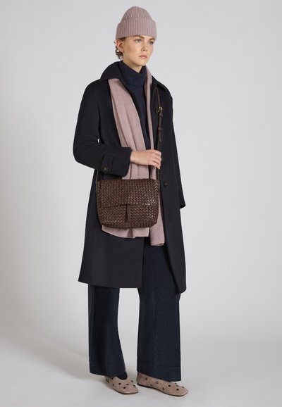 Borsa intrecciata marrone, cappotto blu, sciarpa rosa, maglione blu, pantaloni larghi blu, scarpe chiare con pois scuri. Aspetto texture e a strati.