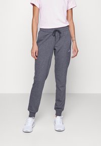 Pantalons de survêtement en coton gris avec taille élastique et cordon de serrage. Comprend des poignets côtelés. Portés avec un t-shirt rose clair et des chaussures de sport blanches.