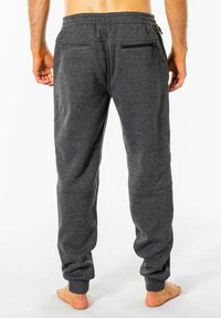 Grå joggebukser lavet af blødt materiale, med en tapered pasform, elastisk talje og to baglomme med sorte lynlåse.