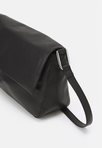 Czarna skórzana kopertówka na nadgarstek z klapką i prostokątną, srebrną metalową klamrą na pasku.