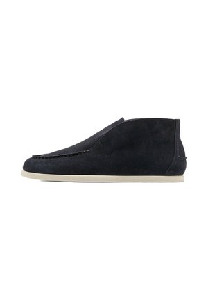 Schwarzer Veloursleder-Slipper mit weißer flacher Sohle und minimaler Naht, seitlich auf weißem Hintergrund.