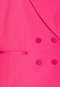 Blazer fuchsia pink à double boutonnage avec une texture lisse, doté de boutons ronds, d'un accent en ruban et d'une coupe ajustée élégante.
