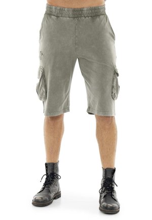 Personne portant un short cargo gris et des bottes noires à lacets, représentée de la taille aux pieds sur un fond blanc.