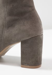 Šedá semišová kotníčková bota s širokým čtvercovým podpatkem. Má hladkou strukturu a bezšvový design na horní straně.