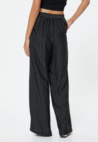 Zwarte wijde broek met een verticale streeppatroon en kleine witte stippen, elastische tailleband en zachte, lichte stof.