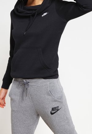Osoba ubrana w czarną bluzę z kapturem Nike i szare spodnie dresowe Nike ze ściągaczem w pasie, pozująca na jednolitym białym tle.