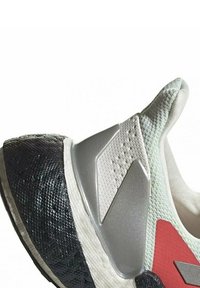 Gros plan sur une chaussure de sport blanche et grise avec une semelle noire texturée et un accent rouge près du talon.