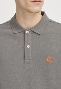 Grå polo t-shirt lavet af struktureret stof med en to-knaps placket med hvide knapper og orange logo broderi på venstre bryst.