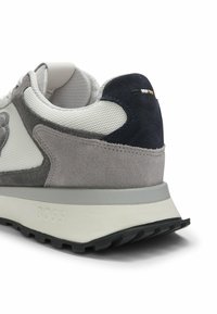 Baskets grises et blanches avec semelle noire, matériaux en suède et mesh, nom de la marque "BOSS" sur la semelle intermédiaire, et petites coutures colorées sur la languette du talon.