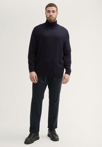Jersey de cuello alto en color navy con un tejido texturizado, combinado con pantalones oscuros y zapatillas negras. El corte es relajado, con mangas largas y puños de canalé.