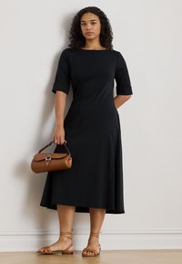 Czarna, do kolan sukienka z rękawami do połowy przedramienia, wykonana z miękkiej tkaniny. Zestawiona z brązową, cylindryczną torebką i płaskimi, paskowanymi sandałami.