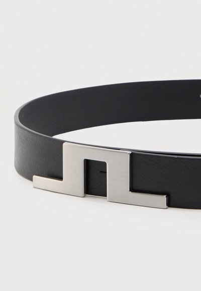 Μαύρη δερμάτινη ζώνη με ορθογώνια ασημένια πόρπη που διαθέτει γεωμετρικό σχέδιο με κοψίματα, εμφανίζεται σε λευκό φόντο.