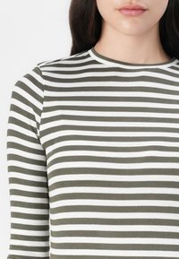 Olive green and white striped ribbed long-sleeve top with a round neckline and fitted design, highlighting a textured fabric.