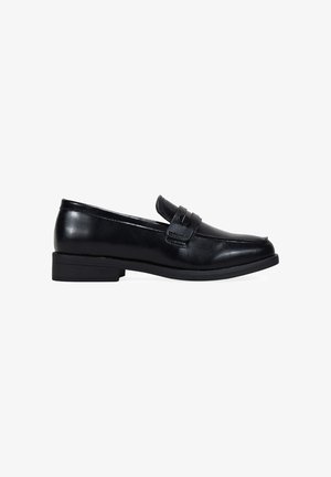 Mocasines de cuero negro con un bajo tacón de bloque, punta redondeada y correa decorativa en la parte superior. Textura suave con un brillo sutil.