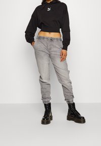 Sudadera negra corta con un logo en la parte frontal, combinada con pantalones de chándal gris ajustados que presentan una cinturilla elástica y puños de punto. Botas negras con cordones.