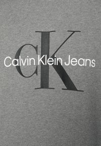 Heather gray sweatshirt featuring a bold black "CK" logo and "Calvin Klein Jeans" text in white, with a smooth, soft texture.