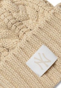 Berretto lavorato a maglia in beige chiaro con motivo a treccia testurizzato e etichetta tessuta con un logo. Il filato morbido offre calore e comfort.