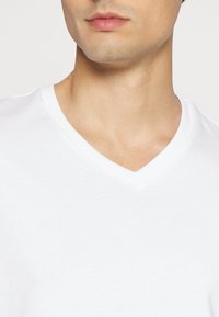 White cotton v-neck t-shirt with a soft texture and clean edges, featuring a simple design and a relaxed fit around the neckline.
